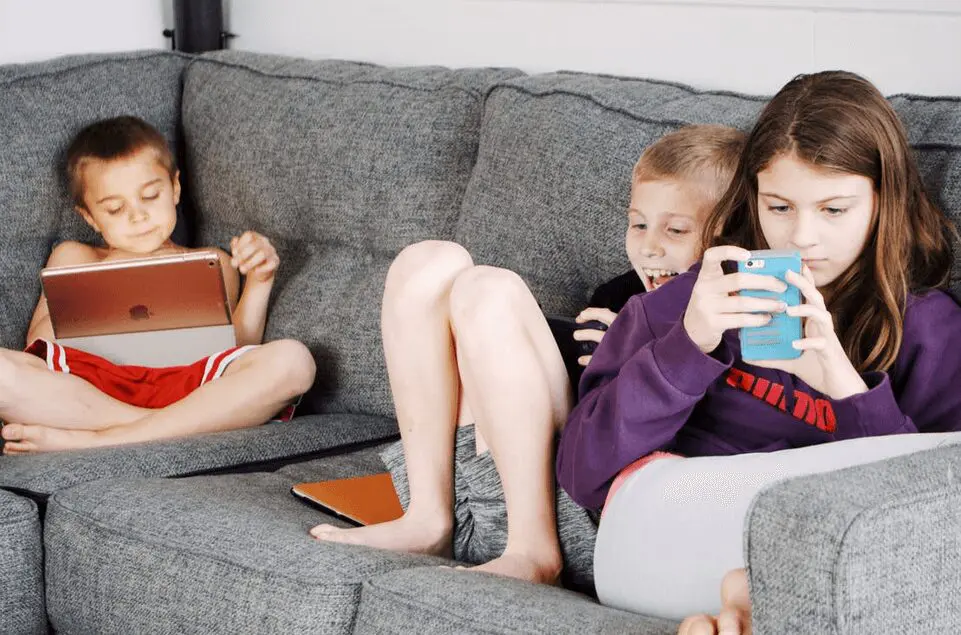 Three Children Using Gadgets on a Sofa