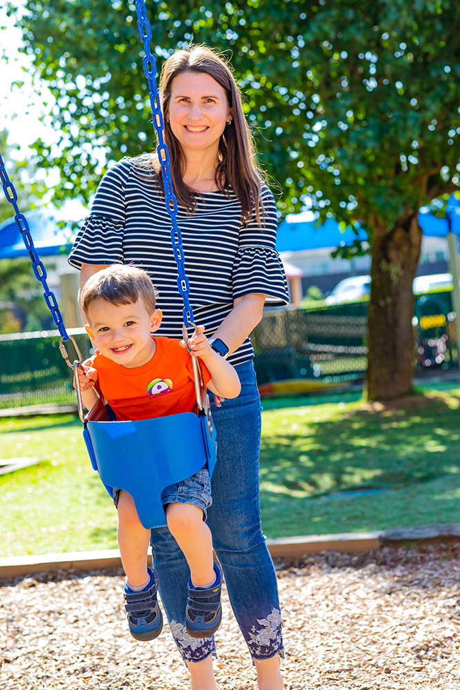 The Daycare Director, Ann Godley playing outside with a boy in a swing.