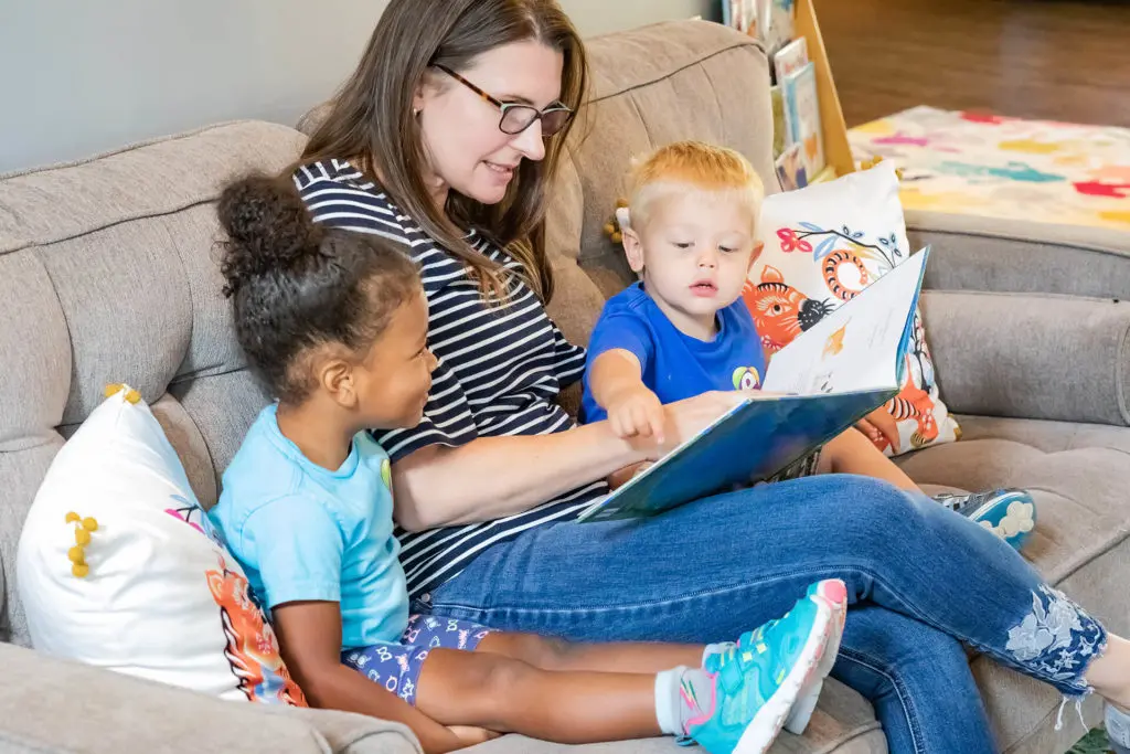 Ms. Ann, the Academy Diretor and Owner is reading to two daycare children on the couch in the reception area